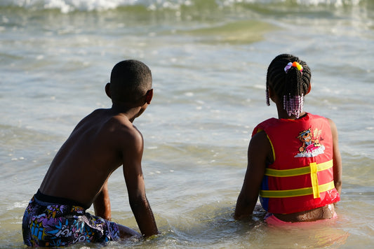 a couple of kids sitting on top of a surfboard in the ocean