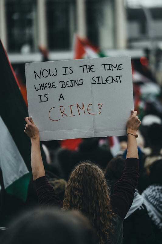 a person holding a sign that says now is the time where being silent is a
