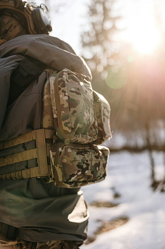 Soldier in camouflage gear with tactical backpack in winter forest.